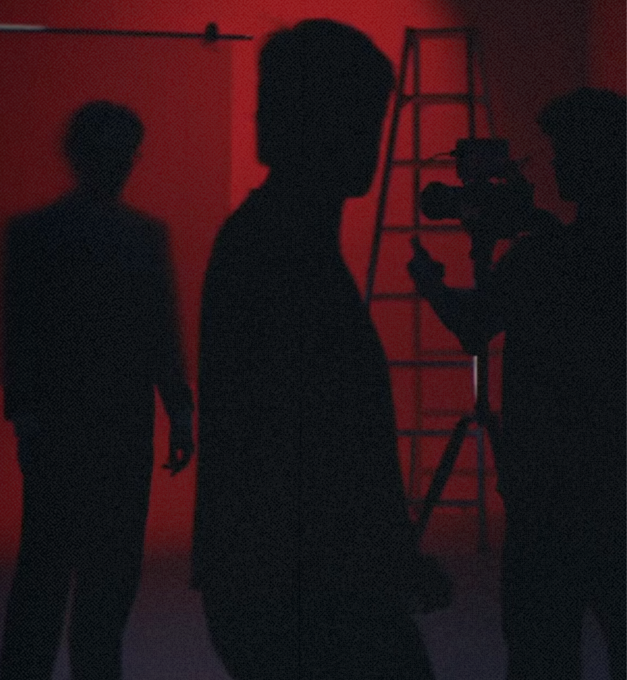 Red-lit studio with silhouetted crew and camera.